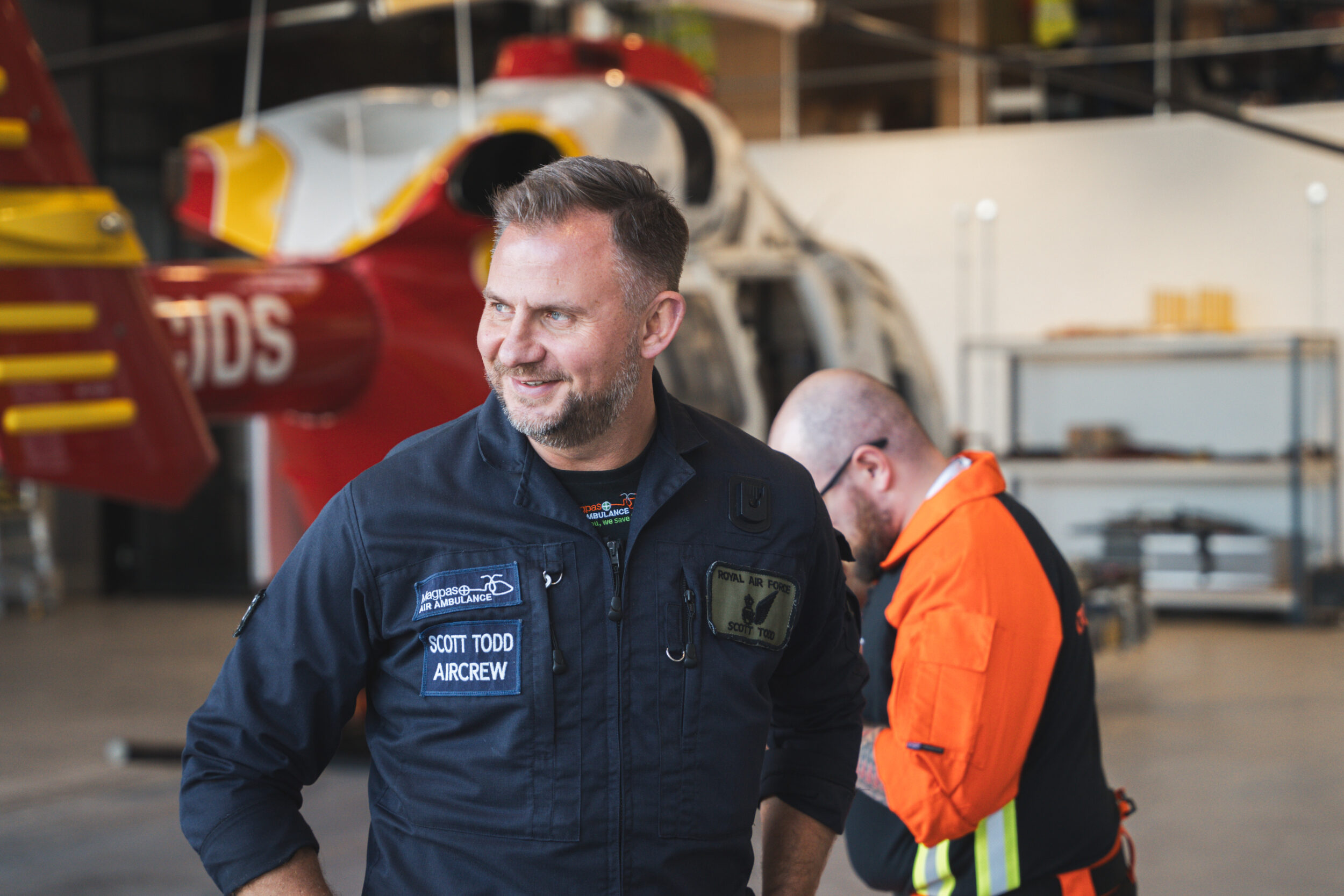 Air ambulance crew laughing in front of a helicopter in a hangar