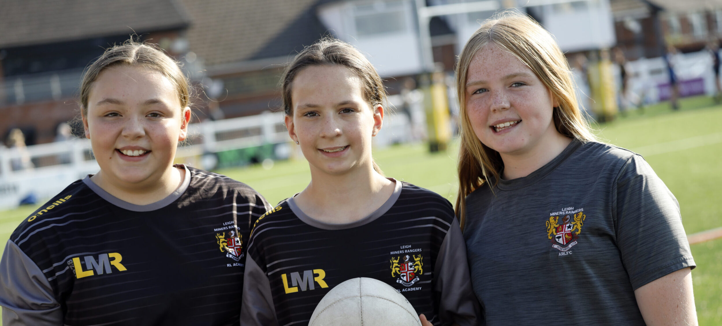 Three girls holding a rugby ball and smiling at a community rugby club